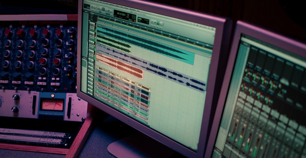 A mastering engineer at a studio console with monitors, outboard gear, and a session on screen