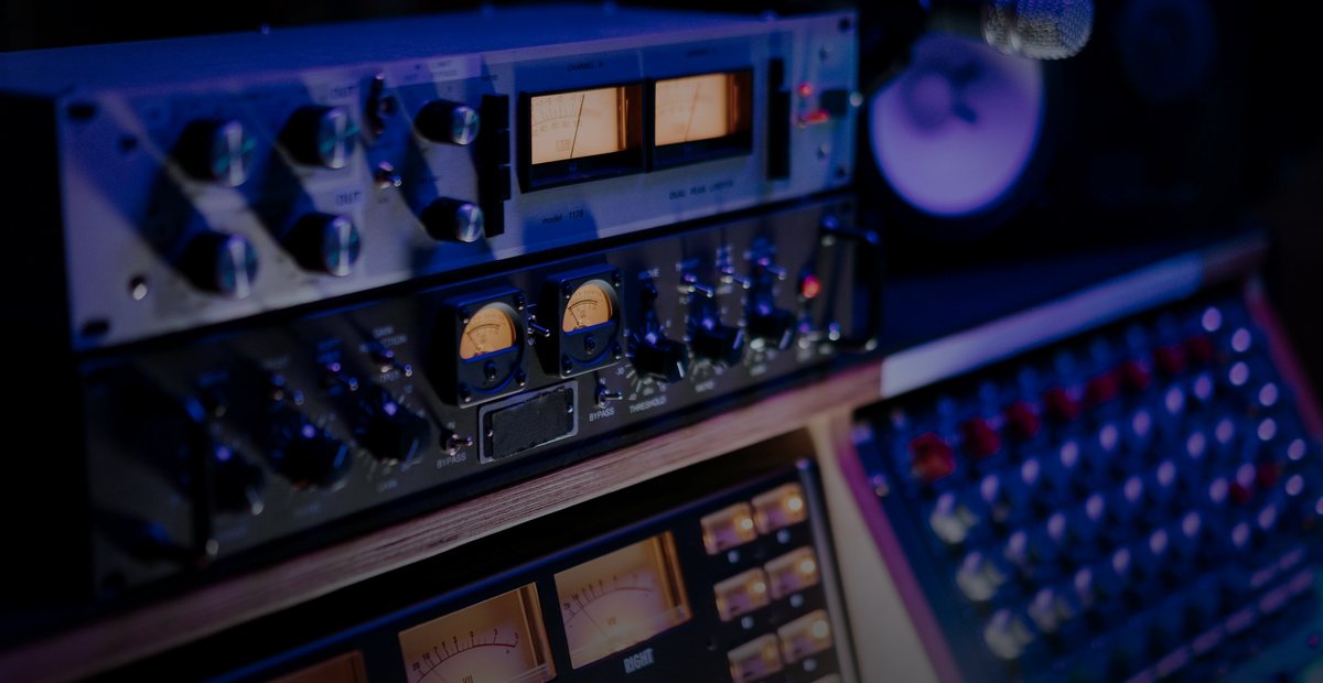A studio rack of outboard gear and a mixing console with VU meters